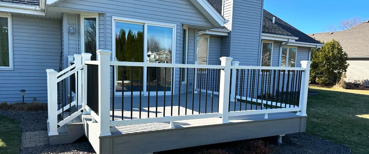 NADRA Certified Deck Safety Inspection 2 Modern composite backyard deck with white and black railings on a gray house in a landscaped yard