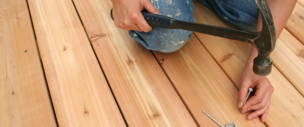 a person using a hammer to nail down new wooden deck boards