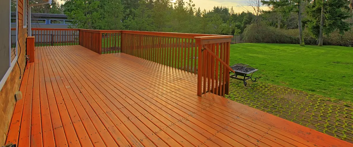 Deck Restoration in Roscoe, IL 2 Spacious wooden deck with red-toned boards and railing in a backyard