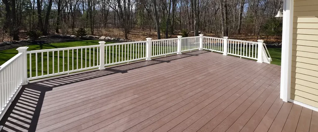 Brown composite deck with white railing in wooded yard
