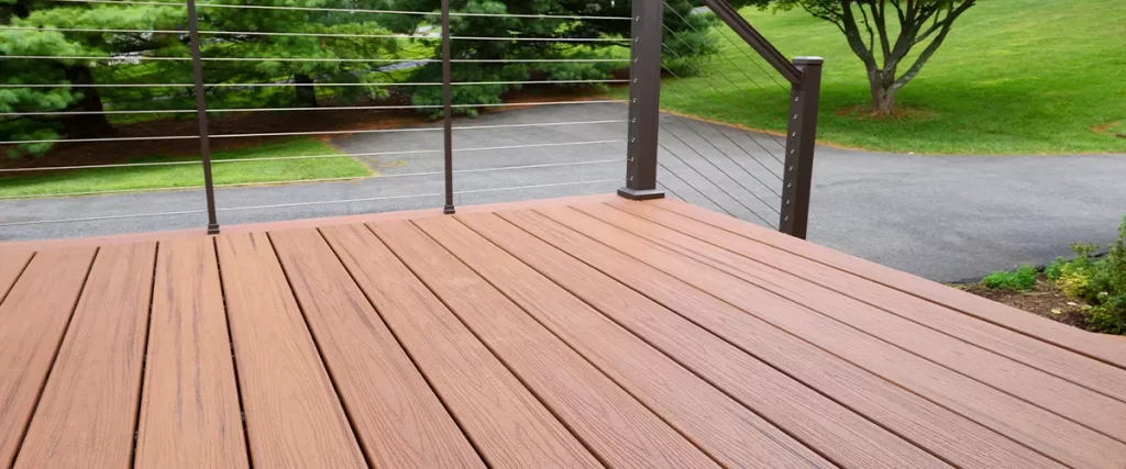 PVC vs Composite Decking: Which Is Better for Your Deck 1 Close-up of a brown composite deck featuring a modern, low-profile design and cable railing leading down to a driveway.