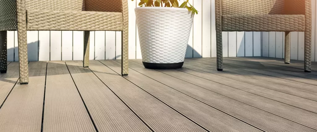 PVC vs Composite Decking: Which Is Better for Your Deck 4 Low-angle view of light gray composite decking showing texture and spacing, with wicker chairs and a white planter resting on the surface.