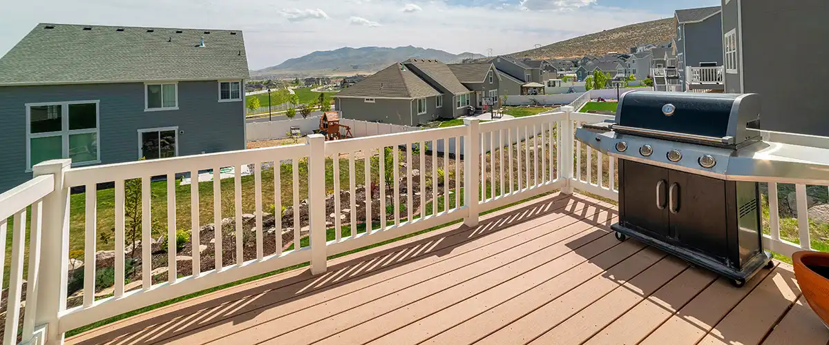 Elevated deck with white railing and grill overlooking suburban neighborhood