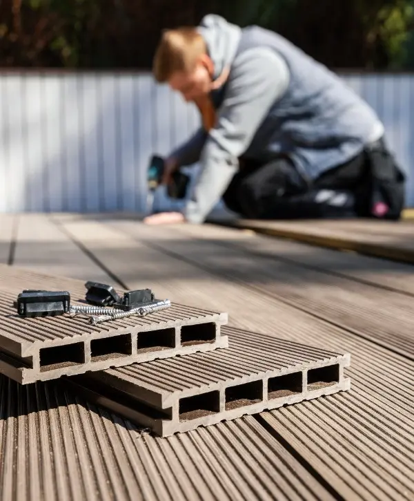 A man is installing wooden decking on a deck, focused on his work with tools and materials around him.