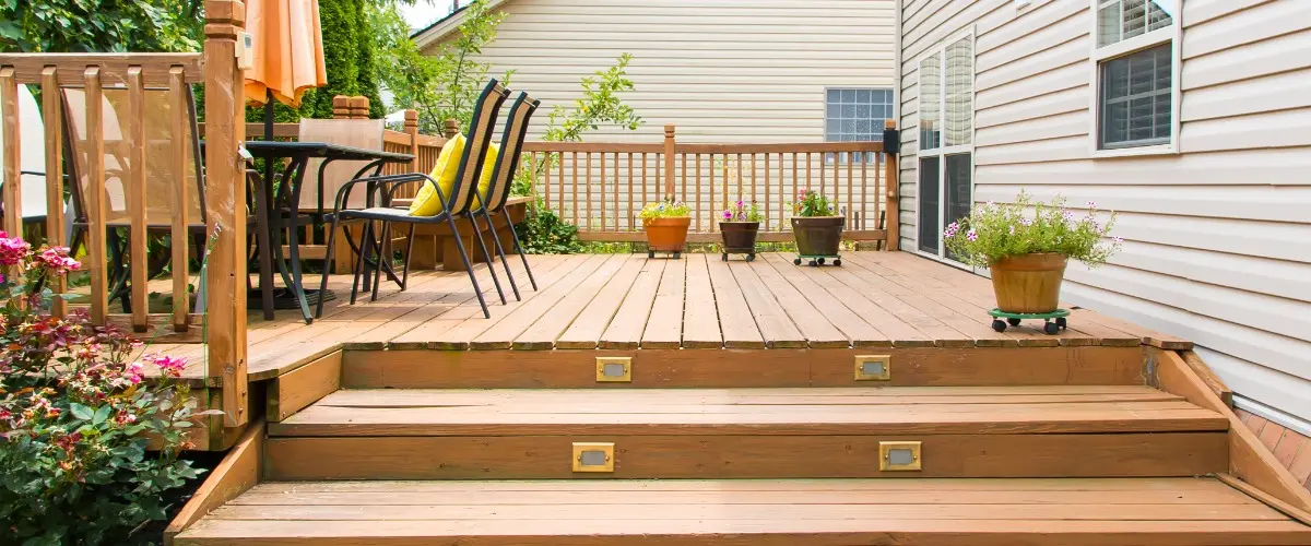 A wooden deck with steps leading down to a spacious patio area.