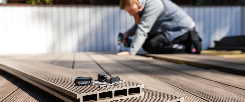 How to Install Composite Decking: A Complete Guide for Your Next Project 1 A man using a power drill to secure the boards to the composite deck frame