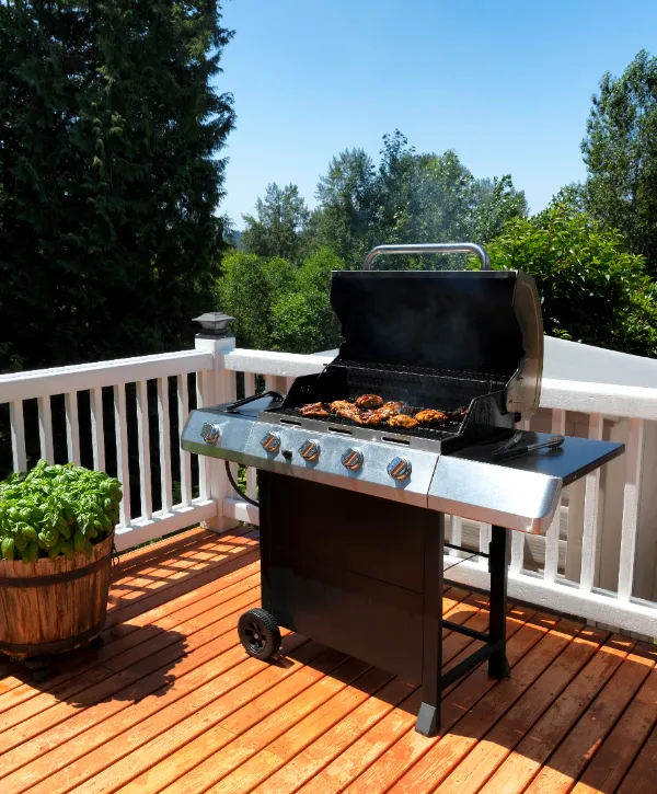 a gas grill being used for cooking on a wooden deck