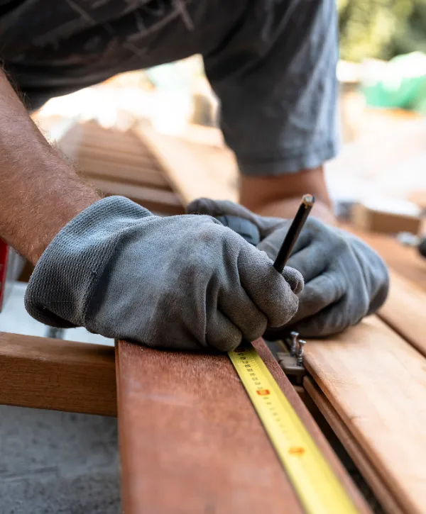 a person measuring and marking a wooden deck board during construction or repair