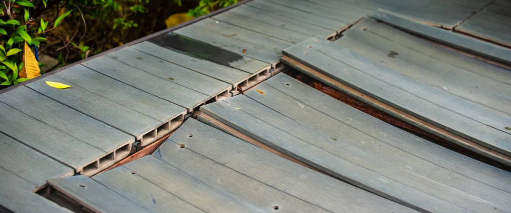A detailed close-up shot showing the cross-section and wood grain texture of weathered gray hollow-core composite decking boards during a repair process.