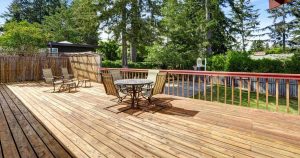 A spacious, sun-drenched wooden backyard deck featuring a round patio table with chairs and a separate lounging area, highlighting why spring and summer are the best time of year to build a deck for outdoor entertainment.